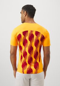 T-shirt athletic a maniche corte di un giallo brillante con un motivo di fiamme color bordeaux sul retro. Realizzato in un tessuto leggero e testurizzato.