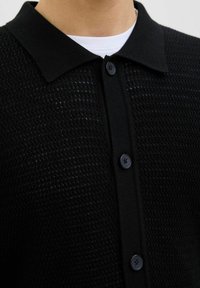 Black knit polo shirt featuring a textured pattern, a structured collar, and black buttons along the front.