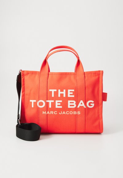Oranje canvas draagtas met witte tekst, voorzien van twee handvatten bovenaan en een afneembare zwarte schouderriem. Gestructureerd ontwerp met zichtbare stiksels.