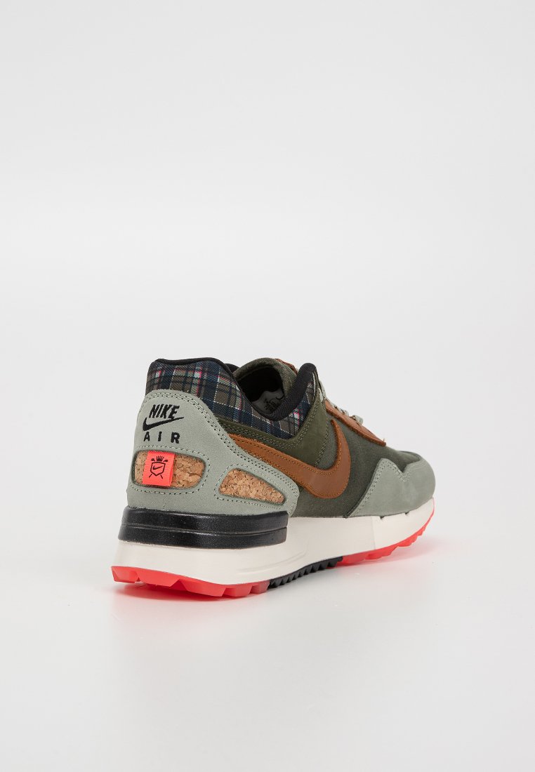Sneakers Nike Air mają oliwkowo-zieloną cholewkę z brązowymi akcentami, podszewkę w kratkę, detale z korka oraz czerwoną podeszwę. Czarna podeszwa środkowa.