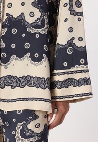 Navy and beige patterned fabric top featuring intricate paisley designs and wide sleeves, with detailed borders and smooth texture.