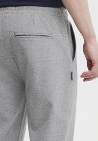 Grå sweatpants med tekstureret stof, elastisk talje og en baglomme med kontrastkant. Nærbillede af bagperspektiv.