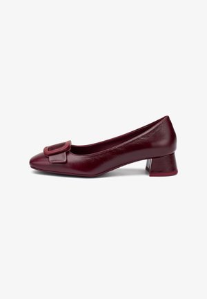 Scarpa da donna bordeaux in pelle con tacco basso, punta squadrata e grande fibbia decorativa frontale, vista laterale su sfondo bianco.