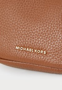 Brown textured leather handbag with a smooth finish, featuring a gold-tone "MICHAEL KORS" logo embossed on the front.