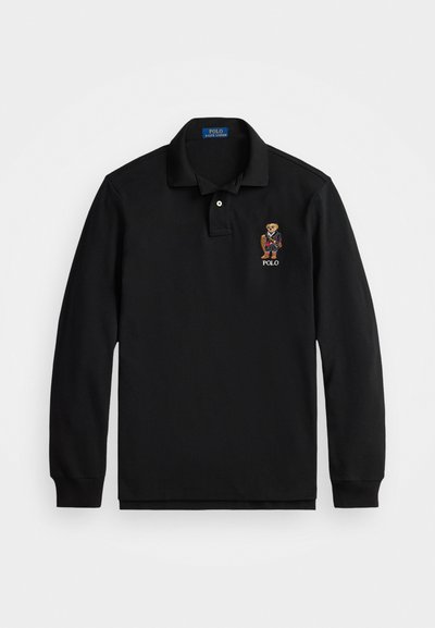 Musthave musta pikkade varrukatega polo särk, mis on valmistatud puuvillast. Omab kaelust, kahte nööpi ja vasakul rinnal tikandina karu logo.