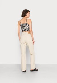 Top cropped com padrão em preto e branco, calças largas bege e sandálias pretas. Detalhes de costura visíveis e etiqueta na parte de trás das calças.
