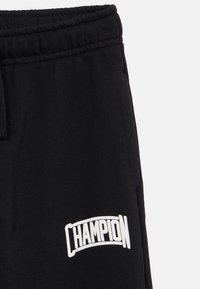 Μαύρη φόρμα από βαμβάκι, με ελαστική μέση και λευκό λογότυπο "CHAMPION" ραμμένο μπροστά. Μαλακή υφή.