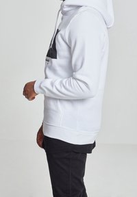 Witte hoodie met een kangoeroezak, capuchon met trekkoord, geribbelde manchetten en een zwarte grafische print aan de voorkant, gecombineerd met zwarte broek.