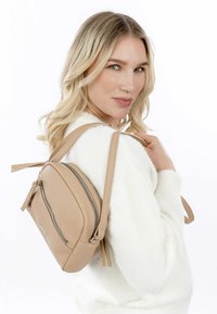 Beige leather sling bag with textured surface and zipper closure. Features adjustable straps and a compact, rounded shape.