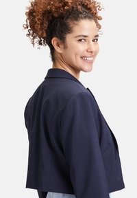 Marineblauwe cropped blazer van gladde stof met een getailleerde pasvorm, voorzien van een geknipt kraag en gestructureerde schouders.