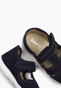 Laivaston kangaskengät, joissa on Velcro-nauha, avoin muotoilu, pehmeä sisäpohja ja valkoinen kumipohja. Sisällä on brändin nimi kohokuvioituna.