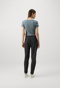 Lyseblå kortermet topp kombinert med skreddersydde svarte bukser, som viser en tettsittende design og jevn tekstur. Fottøyet er hvitt med detaljer.