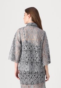 Der silberne Spitzekimono zeichnet sich durch aufwendige Blumenmuster, schulterlange Glockenärmel und einen Kragen aus und präsentiert einen durchsichtigen, strukturierten Stoff.