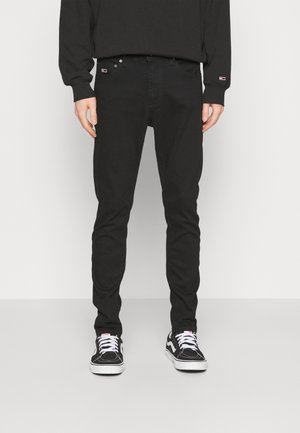 Svarta slim-fit jeans med en klassisk femficksdesign, tillverkade av denim. Bärs med svarta och vita sneakers. Slät textur och minimala accenter.