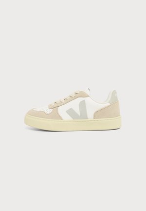 Zapatilla baja beige y blanca con paneles de ante y cuero, suela beige claro y logotipo "V" gris en el lateral.