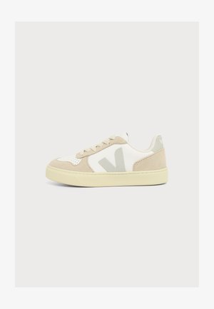 Baskets basses beige et blanches avec des panneaux en suède et cuir, semelle beige clair, et logo "V" gris sur le côté.