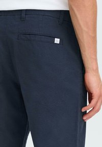 Pantalons en coton bleu marine avec une texture lisse, dotés d'une poche arrière et d'une petite étiquette de logo. Coupe ajustée avec des coutures latérales visibles.