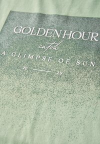 Tissu vert avec un design dégradé et une surface texturée. Du texte blanc indique "HEURE D'OR" et "UN APERÇU DU SOLEIL," avec une plage de dates en dessous.