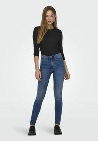 Tynne jeans i mellomblå denim med en falmet vask. Har høy midje, beltehemper og fem lommer. Kombinert med en svart langermet topp.