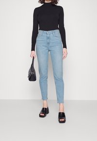 Ljusblå högmidjade jeans, figursydd design, kombinerat med en svart långärmad topp. Svarta slipskor och en strukturerad svart handväska.