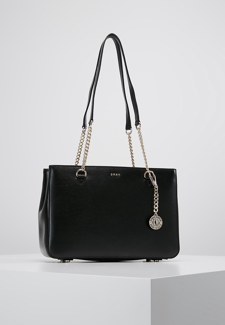 Svart faux läder tote-väska med dubbla handtag, silverkedjeaccent och en DKNY-hänge. Slät textur med en strukturerad design.