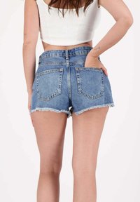 Shorts en denim bleu taille haute avec ourlets effilochés, deux poches arrière et un design classique à 5 poches. Le tissu a un aspect délavé et une texture légèrement usée.