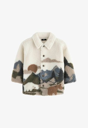 Több színű hegyformájú fleece dzseki fehér, barna és kék árnyalatokban, kordbársony nadrággal és barna sportcipővel párosítva.
