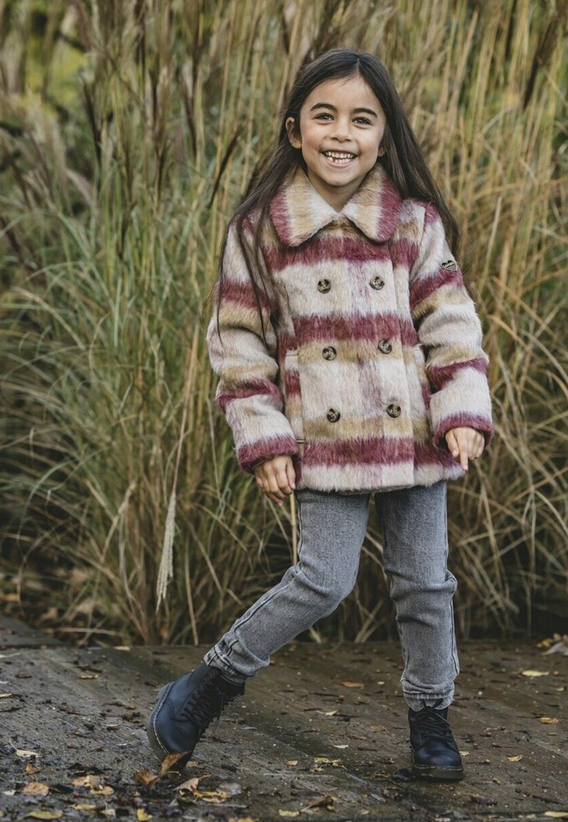 Vachtige dubbel-breasted jas met rode en beige strepen, voorzien van een brede kraag en knopen aan de voorkant, gecombineerd met grijze jeans en zwarte laarzen.