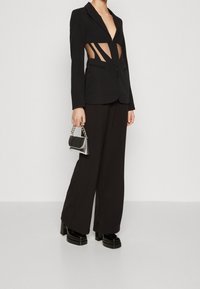 Czarna marynarka z wycięciami, w połączeniu z szerokimi czarnymi spodniami. Stylizacja uzupełnia obuwie na chunky obcasie oraz mała srebrna torebka.