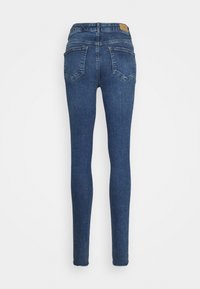 Jeans skinny de denim azul com cintura alta, dois bolsos traseiros e uma textura suave. Apresenta um pequeno logo de couro bege na cintura.