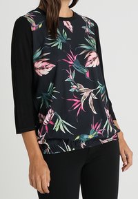 Musta yläosa, jossa on kukkakuosi, 3/4-hihat ja ker gathered helmassa. Valmistettu pehmeästä kankaasta, jossa on elinvoimaisia vihreitä ja vaaleanpunaisia lehtikuvioita.