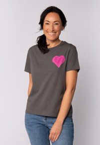 Grijze katoenen T-shirt met korte mouwen, voorzien van een roze hartafbeelding op de linkerborst. Gecombineerd met blauwe jeans. Soepele textuur.