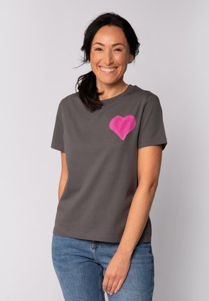 Grijze katoenen T-shirt met korte mouwen, voorzien van een roze hartafbeelding op de linkerborst. Gecombineerd met blauwe jeans. Soepele textuur.