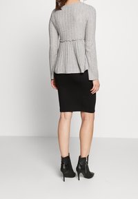 Šedý žebrovaný dlouhý rukáv s nařaseným pasem, spárovaný s černou tužkovou sukní. Modelka má na sobě černé kotníkové boty na podpatku se zipem.