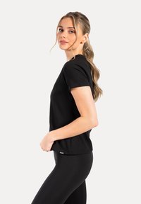 Camiseta negra de manga corta, diseño de cuello redondo, tejido suave, corte relajado, combinada con leggings negros, con una minimalista marca en el dobladillo.