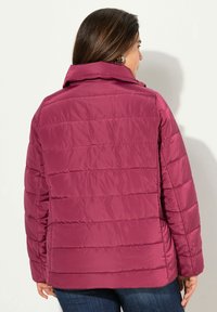 Lyserød pufferjakke med høj krave og horisontal quiltet design. Har en glat, skinnende tekstur og en afslappet pasform.