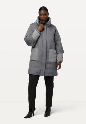 Manteau en mélange de laine gris avec des manches matelassées, deux poches avant, un col haut et une coupe décontractée. Associé à un pantalon noir ajusté et des bottes à talons.
