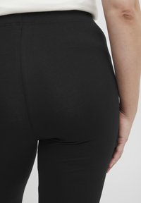 Leggings neri realizzati in tessuto elasticizzato, caratterizzati da una texture liscia e da una vita alta, aderenti al corpo.