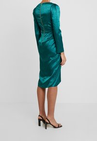 Tarakotafarbene Satin-Kleid mit taillierter Silhouette, langen Ärmeln und einem sichtbaren Reißverschluss auf der Rückseite. Verfügt über ein dezentes, strukturiertes Muster.