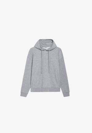 Felpa grigia con cappuccio e cordini, abbinata a pantaloni jogger coordinati. Presenta polsini a coste e sneaker casual con accenti di colore.