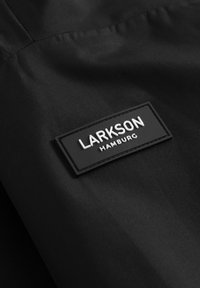 Tissu noir avec un patch rectangulaire noir comportant un texte blanc "LARKSON" et un texte plus petit "HAMBURG" en dessous.