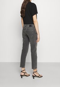 Jean taille haute gris avec coupe droite, cinq poches et une étiquette en cuir noir à l'arrière, associés à des sandales noires à lanières.