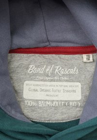 Grå och teal tyg med vinröd akcent; etikett med texten "Band of Rascals", 100% ekologisk bomull, skötselanvisningar; storlekar 110/116.