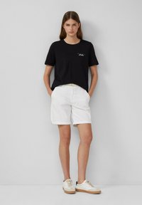 Maglietta nera in cotone con maniche corte e dettagli ricamati bianchi, abbinata a pantaloni corti bianchi in cotone e sneakers beige. Design semplice.