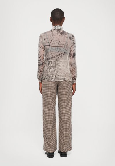 Sheer blouse with a detailed architectural print in soft tones, paired with high-waisted, wide-legged houndstooth trousers and black shoes.