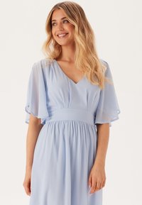 Ljusblå, flödande klänning med V-ringning, korta svallande ärmar och elastisk midja. Tyget verkar mjukt och lätt.