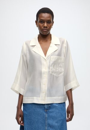 Krēmbaltas krāsas blūze ar izgrieztu apkakli, pusgarām piedurknēm, priekšējiem pogām un kabatu ar smalku izšuvumu. Mīksts, viegls audums.