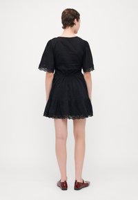 Schwarzes Baumwollkleid mit kurzen Puffärmeln, taillierter Taille und gestuftem Rüschensaum. Verfügt über bestickte Spitzenbesätze entlang der Ärmel und des Saums.