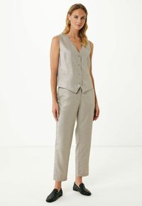 Ljusgrå väst med V-ringning, framknappar och två fickor, som matchas med skräddarsydda byxor av texturerat tyg. Bärs med svarta loafers med prickar.