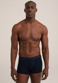 Tumši zili bokseršorti ar mīkstu jostasvietu. Audumam ir gluda tekstūra un pieguļošs dizains, kas izceļ elegantu siluetu.